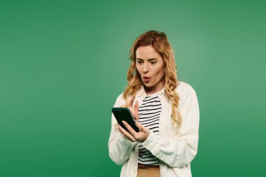 A beautiful woman with curly hair expresses surprise while checking her phone, set against a vibrant green background. clipart