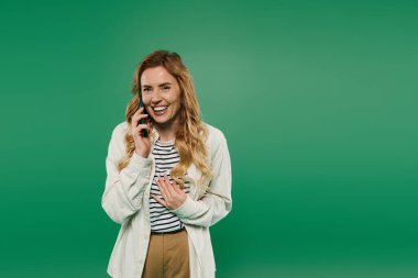 Neşeli bir kadın, günlük kıyafetler içinde telefonuyla konuşurken gülümsüyor, anın tadını çıkarıyor..