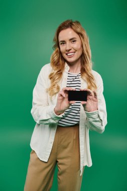 Kıvırcık saçlı bir kadın yeşil bir arka planın önünde elinde siyah bir kartla gülümsüyor..