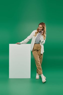 Kıvırcık saçlı güzel bir kadın, boş bir yüzeye yaslanırken telefonla konuşmaktan zevk alır..