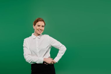 Zeki beyaz tişörtlü profesyonel bir kadın yeşil bir zeminde güler yüzlü bir şekilde duruyor..