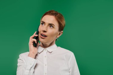 Beyaz gömlekli kendine güvenen bir kadın akıllı telefonuyla bağlanıyor. Çevresi canlı yeşil bir fon ile çevrili..
