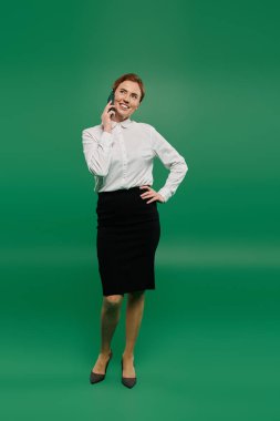 Beyaz gömlekli ve siyah etekli kadın telefonda konuşurken gülümsüyor, profesyonelliğini gösteriyor..