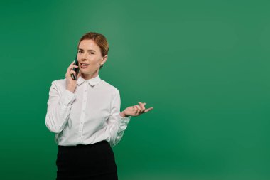 Beyaz gömlekli profesyonel bir kadın telefonda konuşuyor. Uzmanlığını yeşil arka planda sergiliyor..