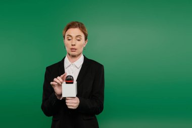 Tarz sahibi siyah elbiseli TV sunucusu, parlak yeşil bir arkaplan karşısında duran bir seyirciyle karşılaşır..