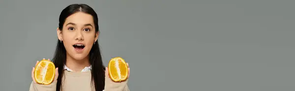 stock image A young, emotional woman joyfully holds halved oranges, creating a vibrant visual in her attire.