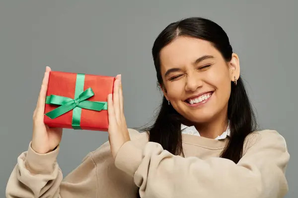 stock image The emotional young woman beams with happiness while showcasing a festive gift in her hands.