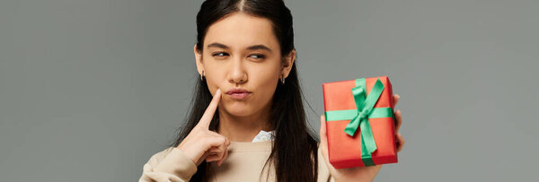 Эмоциональная молодая женщина в модном наряде игриво считает неожиданный подарок, который она держит.