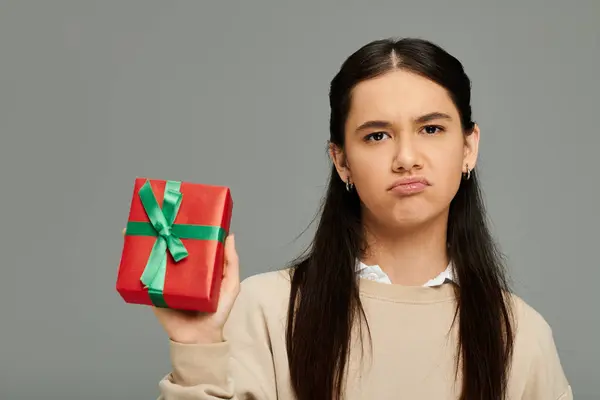 stock image A young woman stands in fashionable attire, revealing her uncertainty as she holds a gift.