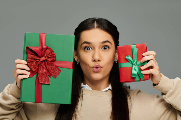 Молодая женщина выражает радость, держа два красиво завернутых подарка, демонстрируя радость.