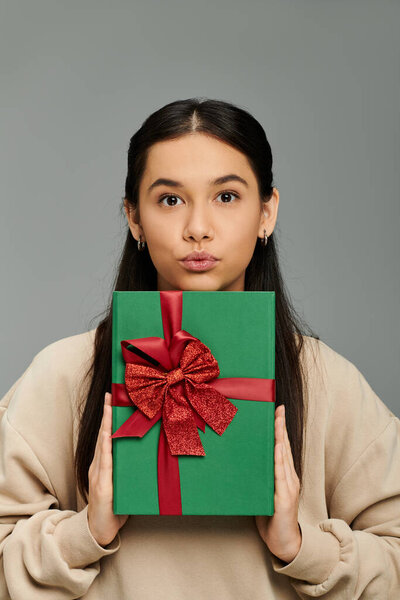 Эмоциональная молодая женщина держит красиво завернутый подарок, демонстрируя свое ожидание и радость.