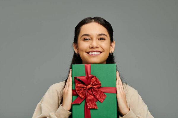 Ее яркая улыбка излучает радость, когда она с гордостью держит красиво завернутый зеленый подарок.