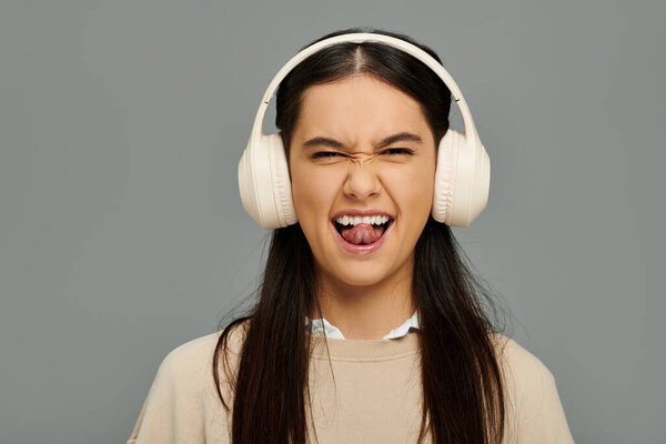 A young woman, stylishly dressed, joyfully makes a playful face while listening to music.