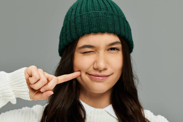 Молодая женщина в модной одежде игриво подмигивает, прикасаясь к щеке.