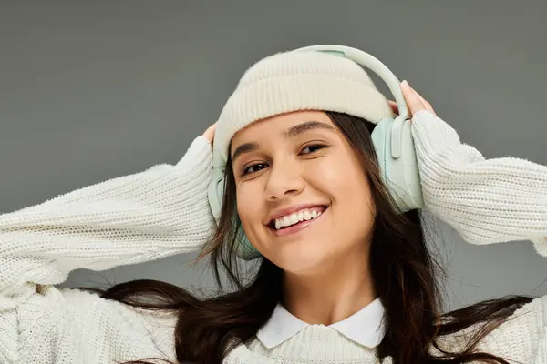 stock image A cheerful young woman wearing a cozy sweater and headphones smiles with delight, embracing music.