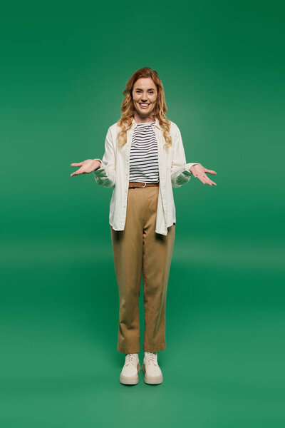 A cheerful woman with curly locks showcases her casual style against a bright green background while gesturing.