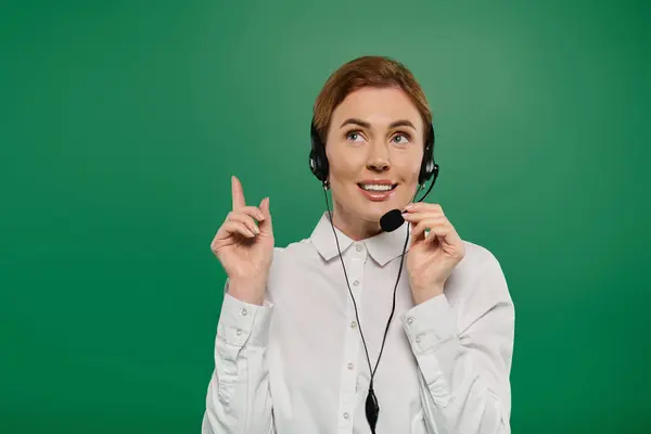 stock image A professional woman in a white shirt engages with customers, confidently using a headset against a green backdrop.