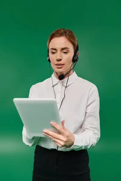 stock image A call center professional in formal attire is actively engaging with a tablet, set against a green background.