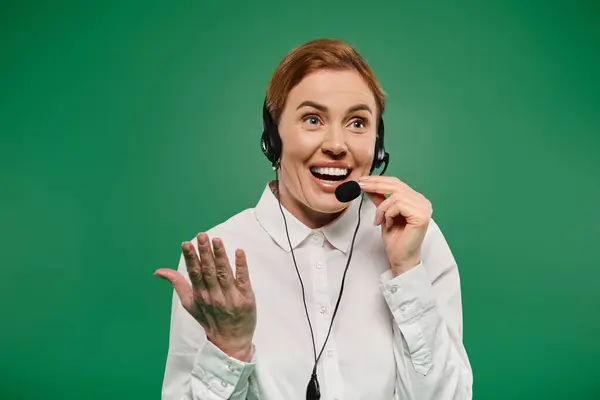 stock image A lively woman in formal wear shares insights while wearing a headset against a vibrant green backdrop.