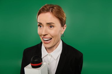 TV sunucusu dinleyicilerle canlı yeşil bir fon karşısında konuşurken sıcak bir şekilde gülümsüyor..