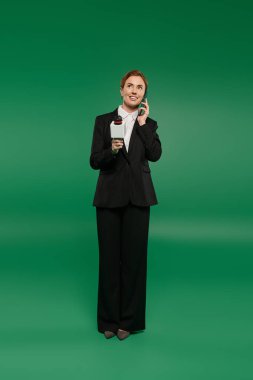 Resmi siyah giyimli şık bir TV sunucusu, yeşil bir arkaplan karşısında telefonla izleyicilerle meşgul oluyor..