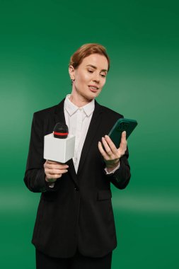 Parlak siyah giysiler içinde sunucu elinde bir mikrofon ve akıllı telefon tutuyordu..