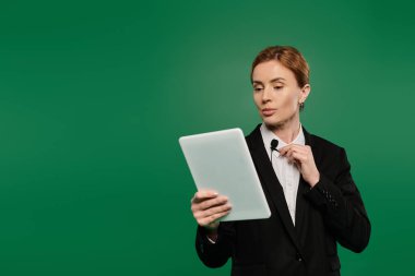 Zarif siyah resmi kıyafetli sunucu, elinde bir tablet, elinde karizma gösterirken izleyicilerle etkileşime girer..