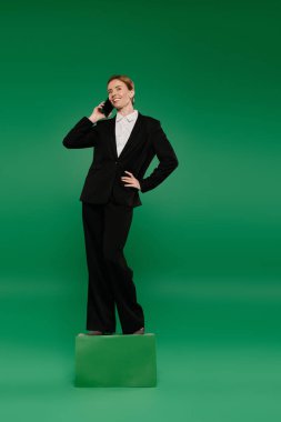 A confident TV presenter stands on a platform, discussing topics live with a phone against a bright green backdrop. clipart