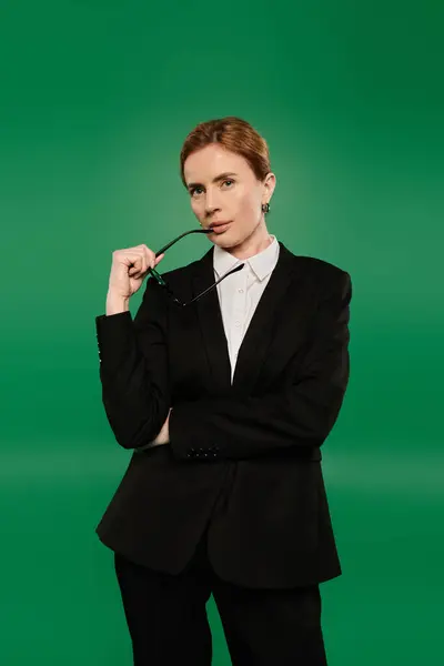 stock image A poised TV presenter in sleek black attire strikes a thoughtful pose against a vibrant green background.