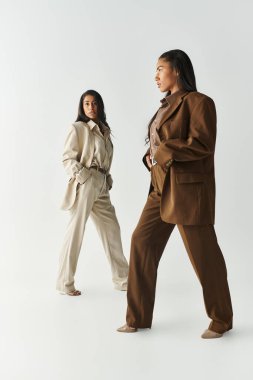 İki genç kadın, minimalist bir stüdyoda moda seçimleri sergiliyor..