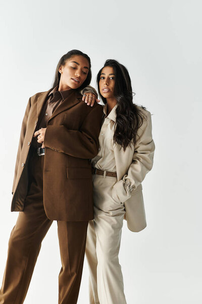 Two fashionable young women stand closely, showcasing their trendy suit ensembles elegantly styled.