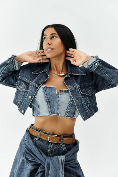 Модная молодая женщина приспосабливает свой стильный джинсовый наряд, изящно позируя в помещении.
