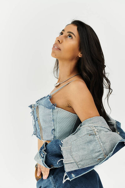 Молодая женщина демонстрирует свою модную джинсовую одежду, в то время как излучает уверенность в себе.