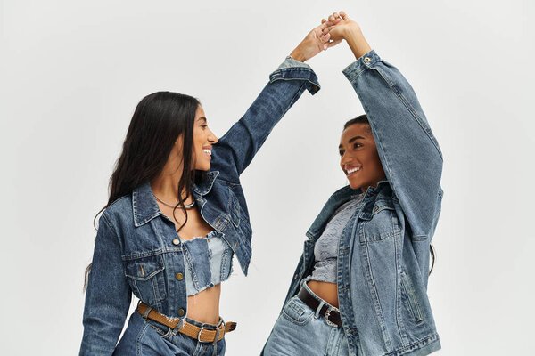 Two fashionable friends joyfully share a playful moment while showcasing their trendy outfits.