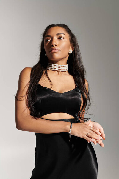 A fashionable young woman poses gracefully, highlighting her stylish black dress and elegance.