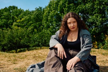 A confident plus size woman sits gracefully in a sunlit field, embraced by nature. clipart