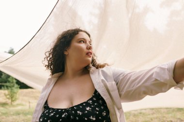 A beautiful plus size woman stretches her arm in a sunlit field, surrounded by natures tranquility. clipart