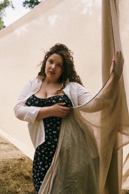 Yumuşak kumaşla kaplanmış, kendine güveni ve güzelliği somutlaştıran, dingin bir alanda duran iri yarı bir kadın..