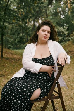 A beautiful plus size woman sits gracefully on a chair in a tranquil field, surrounded by nature. clipart