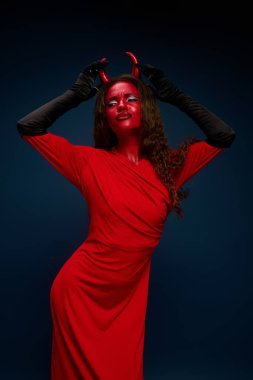 Cesur kırmızı kostümlü büyüleyici bir kadın oyuncu ve şeytani tarzıyla hava atıyor..