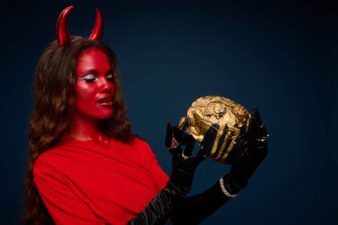 Kırmızı ve siyah Cadılar Bayramı kıyafetli çarpıcı bir figür büyüleyici bir şekilde süslenmiş kafatasına hayran..