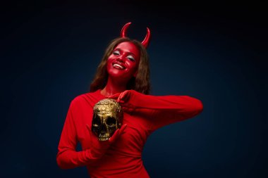 A striking woman in a red costume poses with a golden skull, embodying Halloween spirit. clipart