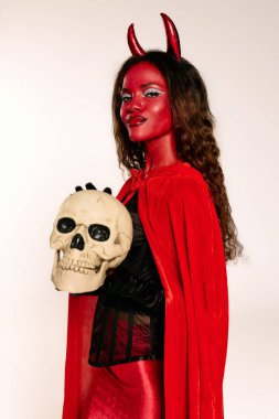 A stunning woman in a bright Halloween costume poses confidently with a skull. clipart