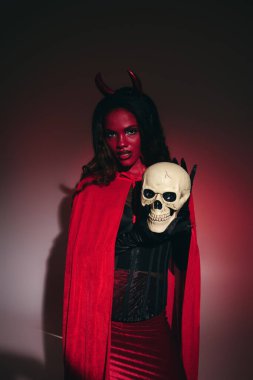 Göz alıcı güzellikte bir kadın şeytani boynuzları ve kafatasıyla Cadılar Bayramı kostümünü sergiliyor..