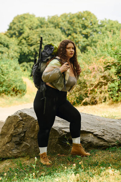 A plus size woman stands among vibrant greenery, fully embracing nature and adventure.