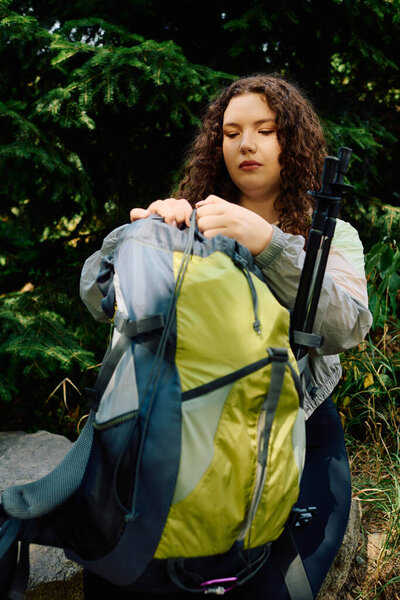 Красивая женщина плюс размер организует свой рюкзак среди пышной зелени, обнимая природу спокойствия.