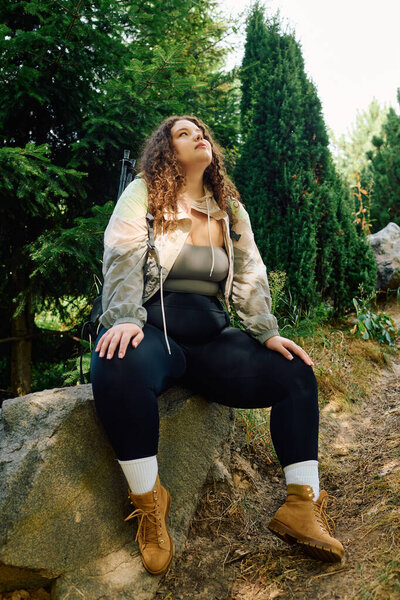 A confident plus size woman sits on a rock, enjoying the peaceful, lush greenery.