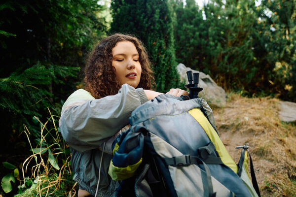 A cheerful woman in a forest enjoys nature while preparing for an outdoor adventure.