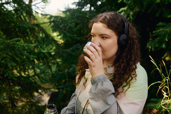 A lovely woman savors a warm beverage amidst lush greenery, embracing serenity in nature.