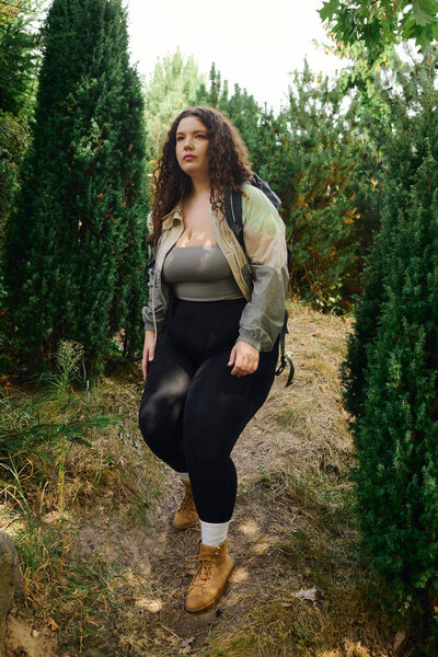 A confident plus size woman enjoys a peaceful stroll among vibrant green trees.